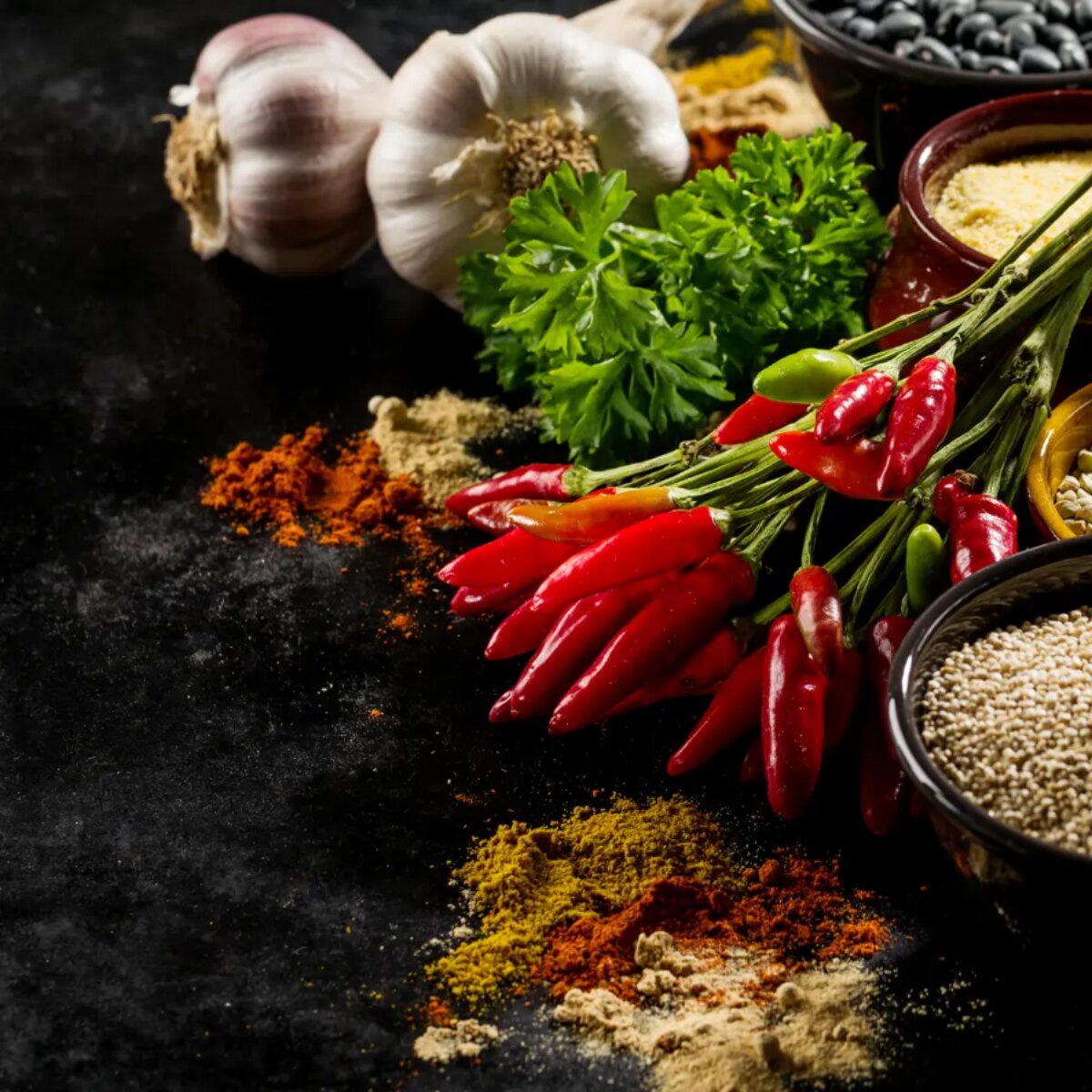 Chillies, garlic, herbs and ground spices on a dark bench